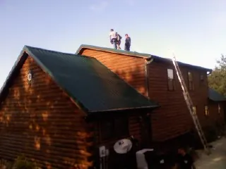 Crew on the ridge of a green metal roof on a two story log home in Zionsville
