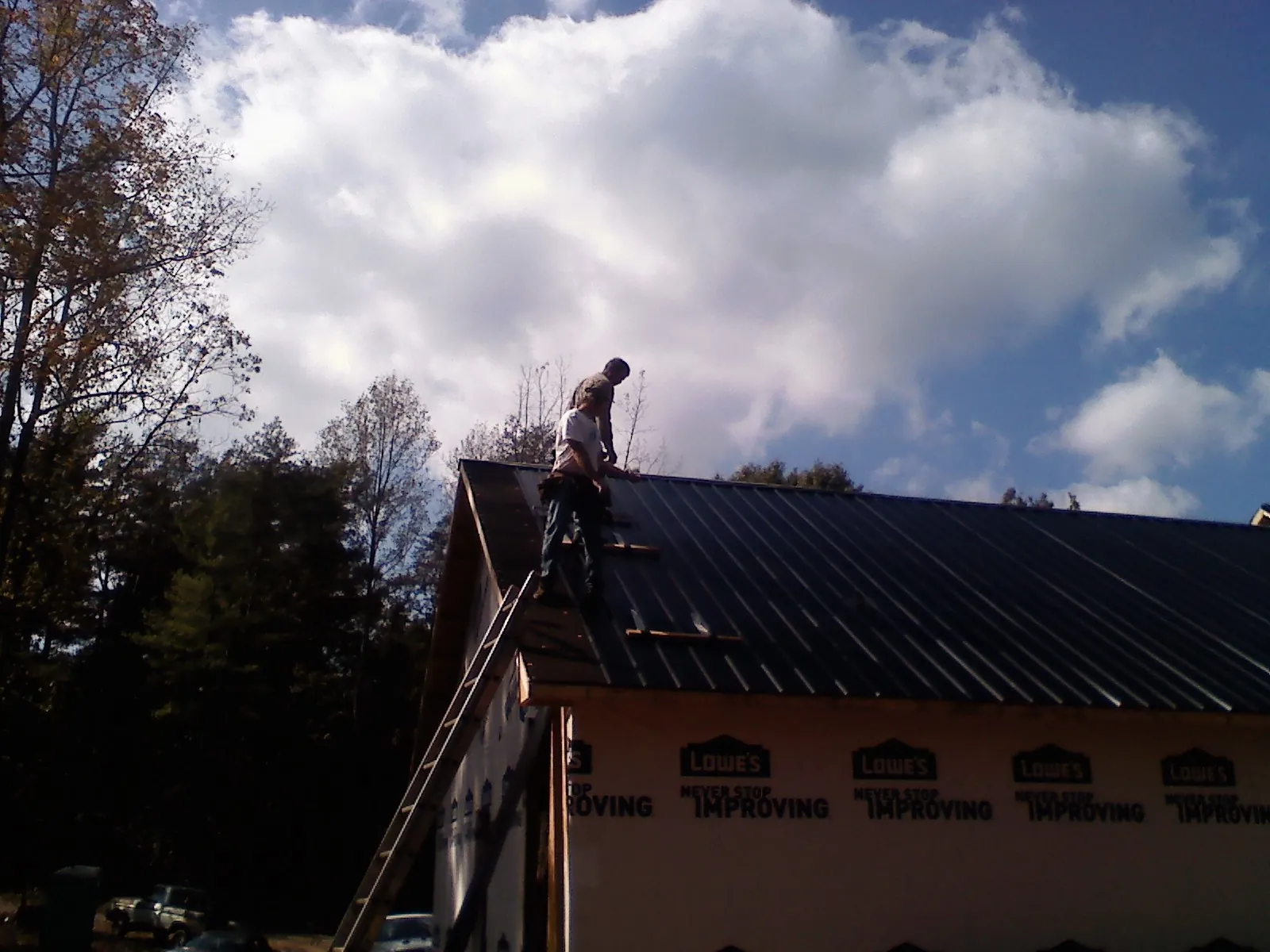 Roofer fastening dark metal panels high against a cloudy sky, from a Roof Inspection job in Zionsville