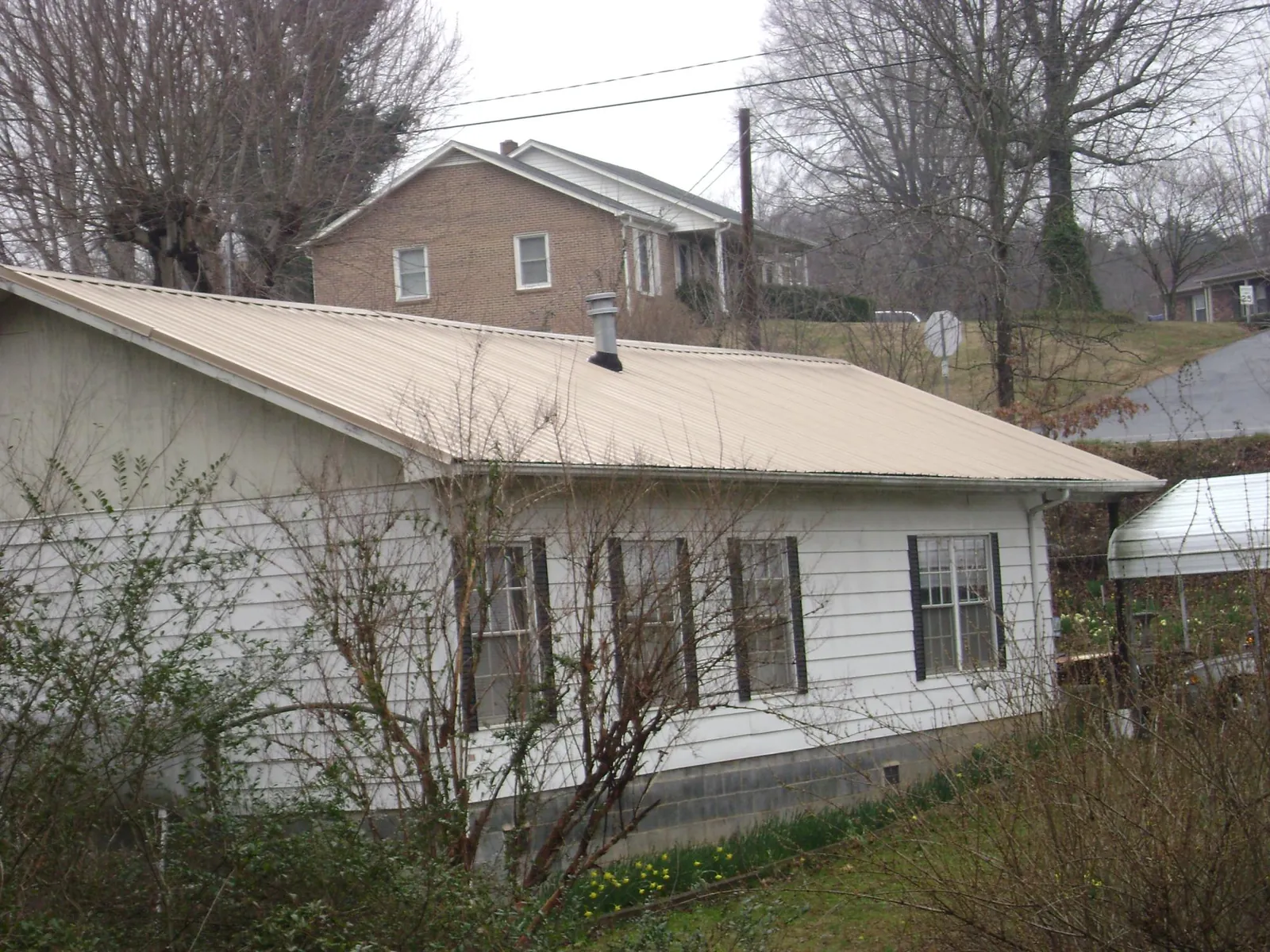 Tan metal roof on a white sided house set into a hillside — Commercial Roofing by Roofing Brothers in Zionsville